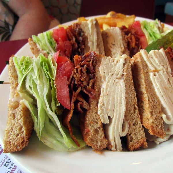 A Morristown Diner club sandwich with turkey, bacon, lettuce, and tomato, served with fries and a pickle.