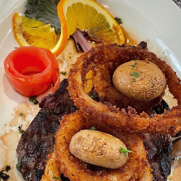 Morristown Diner's steak with crispy onion rings, mushrooms, tomato, and orange slices on a white plate.