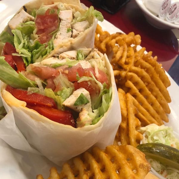 Chicken wraps with lettuce and tomatoes, served with waffle fries, coleslaw, and a pickle.