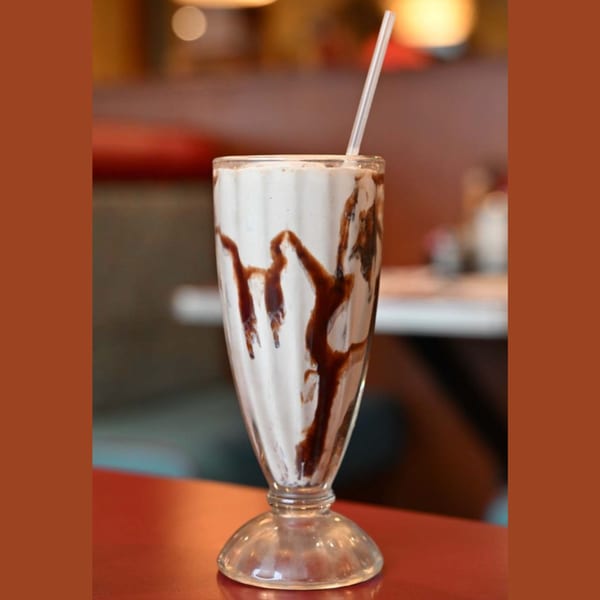 A chocolate milkshake with chocolate syrup drizzled inside, served in a tall glass with a straw.