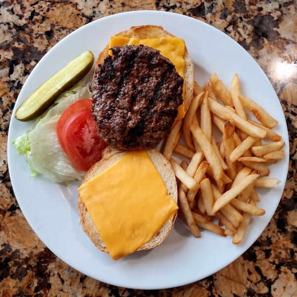 Grilled cheeseburger with lettuce, tomato, pickle, and French fries on a white plate.